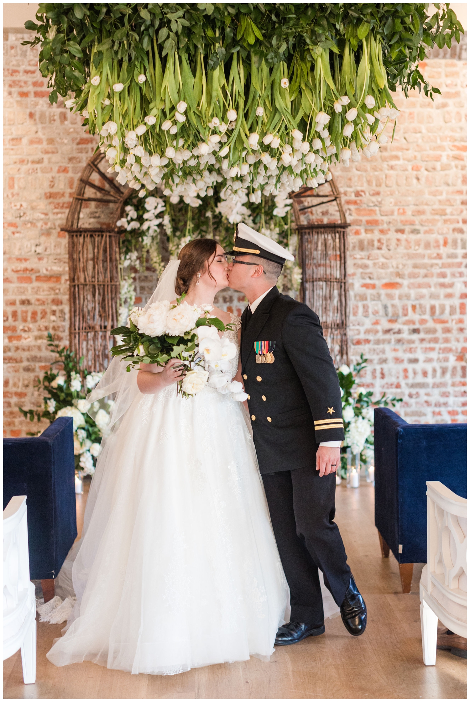 bride and groom kissing under hanging florals inside Merchants Hall