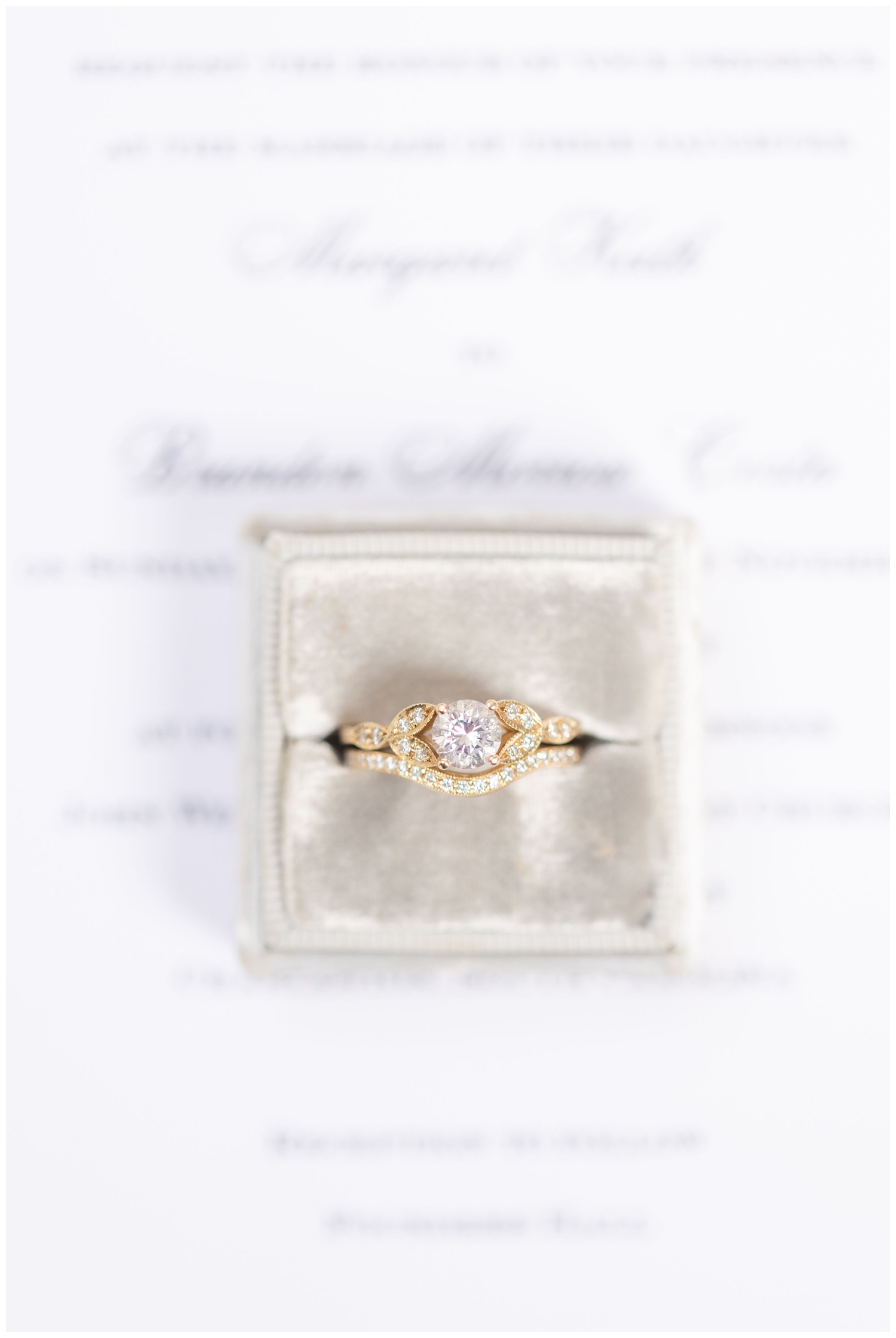 close up of diamond wedding ring sitting on all white invitation