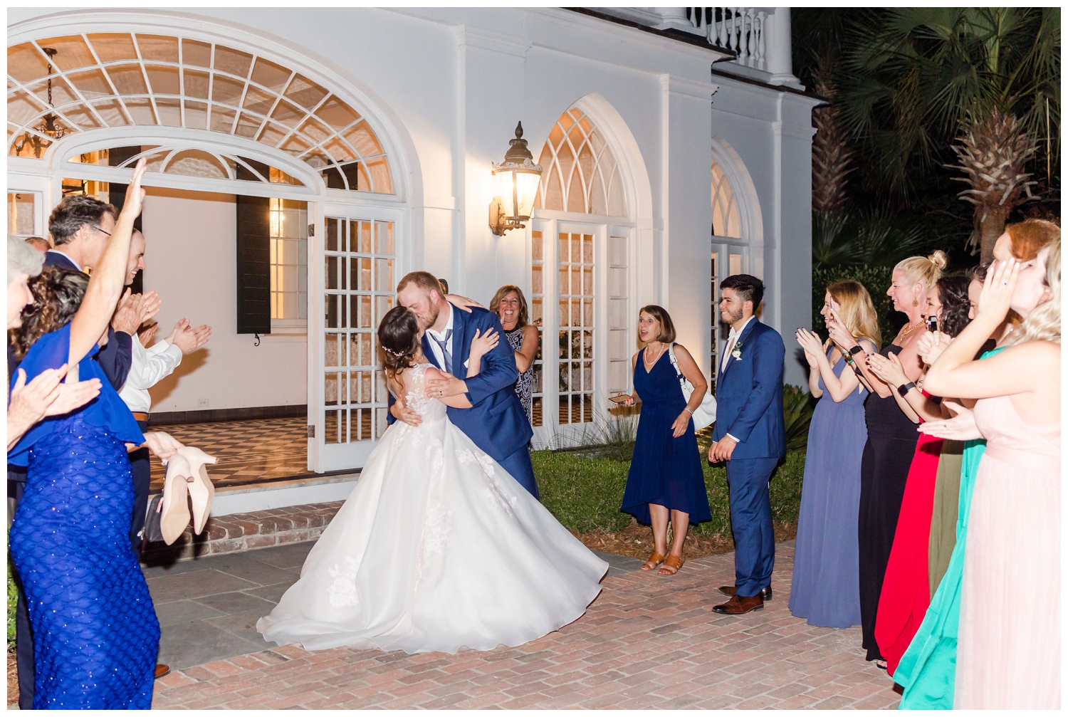 bride and groom kissing with guest cheering on during grand exit