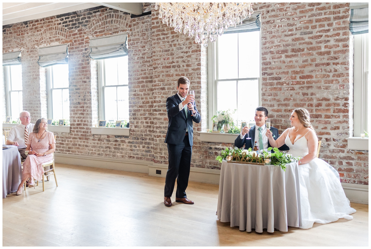 groom toasting bride and groom sitting at sweetheart table Charleston Merchants Hall Reception