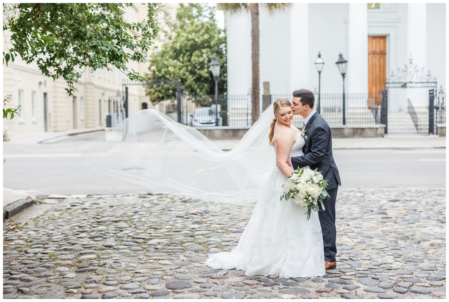 bride and groom kissing with veil toss outside Charleston Merchants Hall