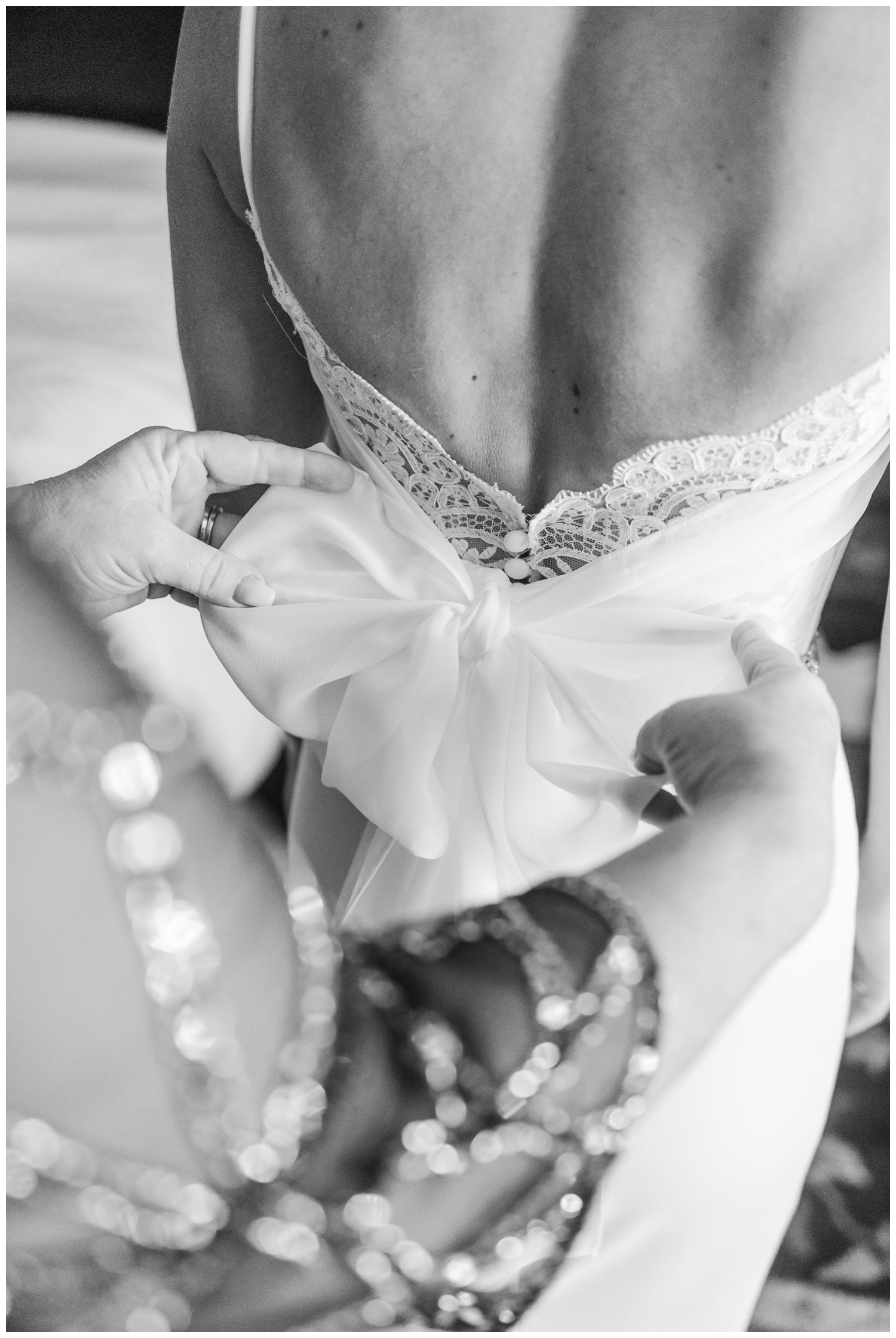 black and white photo of hands straightening bow back of wedding gown