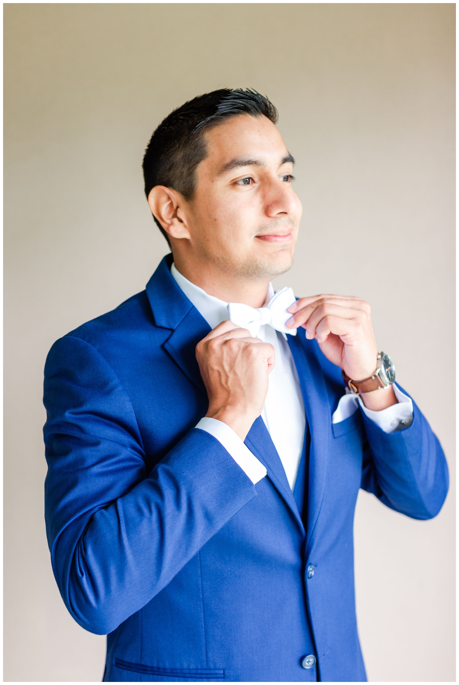 groom in blue suit straightening white bow tie